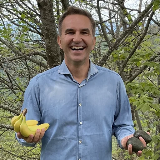 Patrick Struebi smiling among the trees, bananas in one hand and avocados in the other